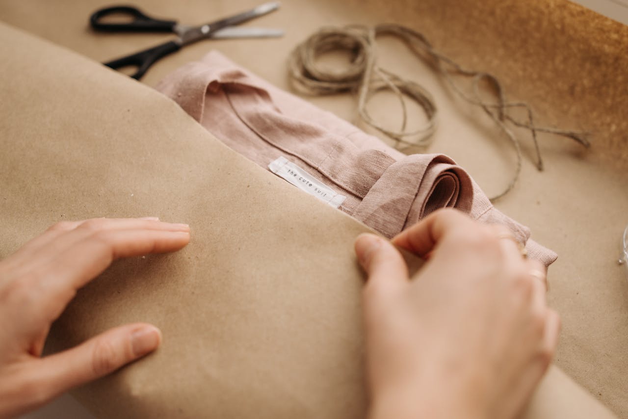 Close-up of hands wrapping a linen shirt with twine, showcasing craftsmanship and sustainable fashion.